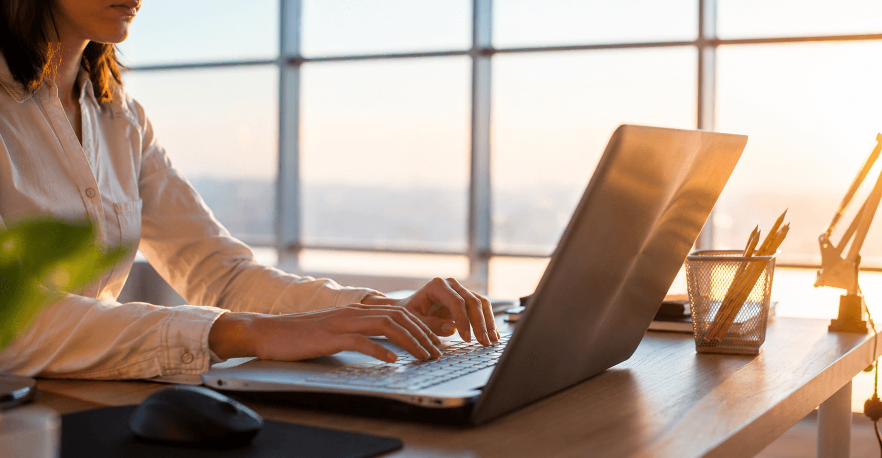 Femme travaillant sur un ordinateur portable à un bureau à domicile, la lumière du soleil entrant par une grande fenêtre
