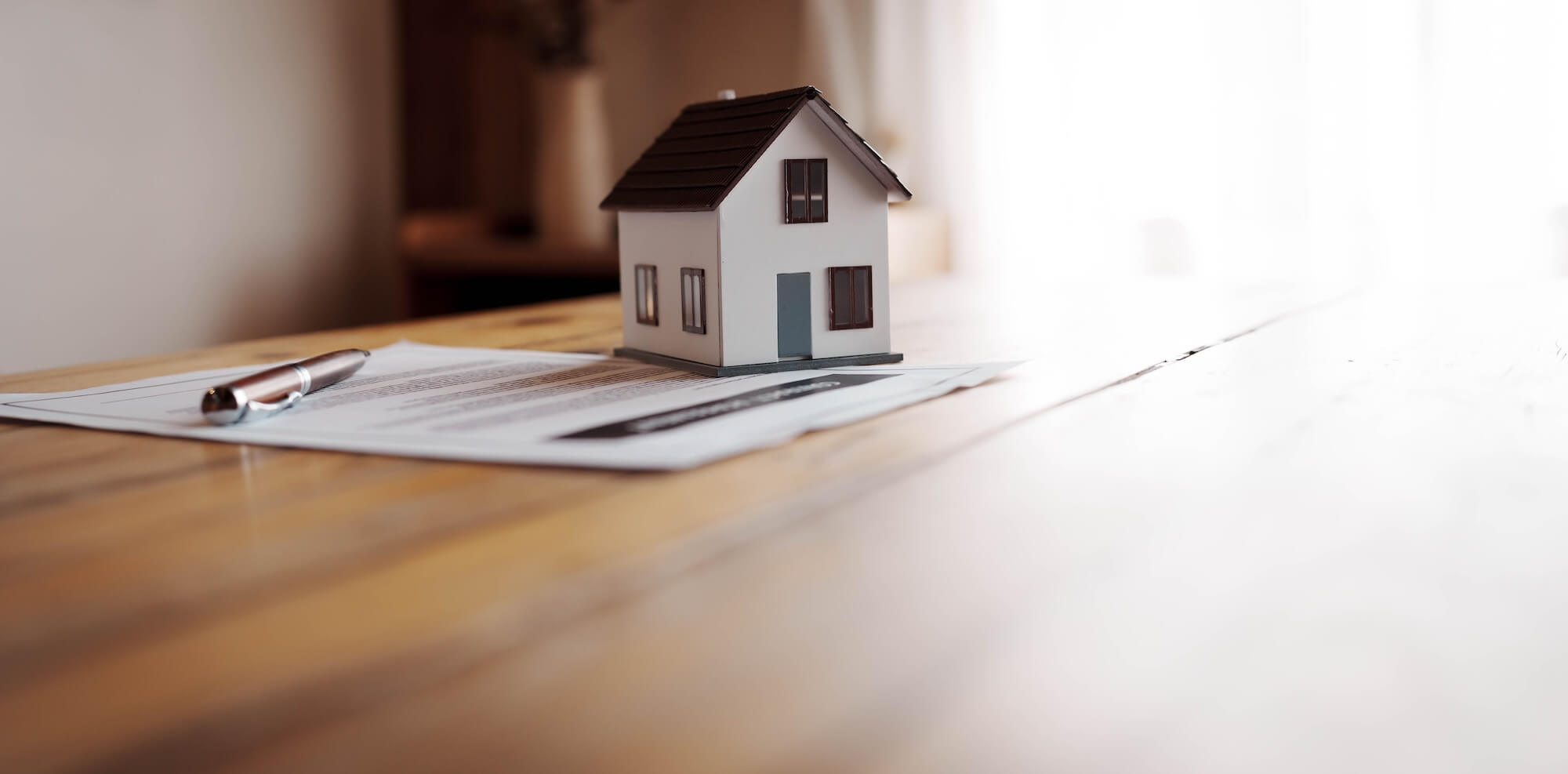 Maison miniature et stylo sur un contrat hypothécaire, posés sur une table en bois