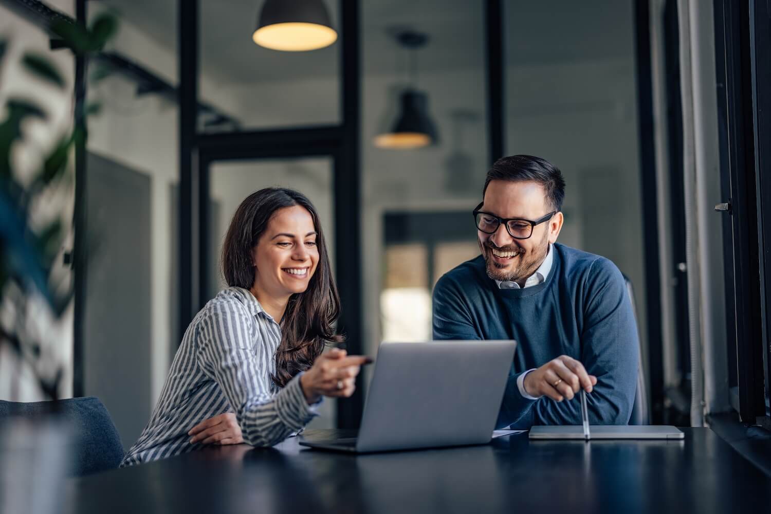 Un couple discute d'un contrat de travail devant un ordinateur portable dans un bureau moderne